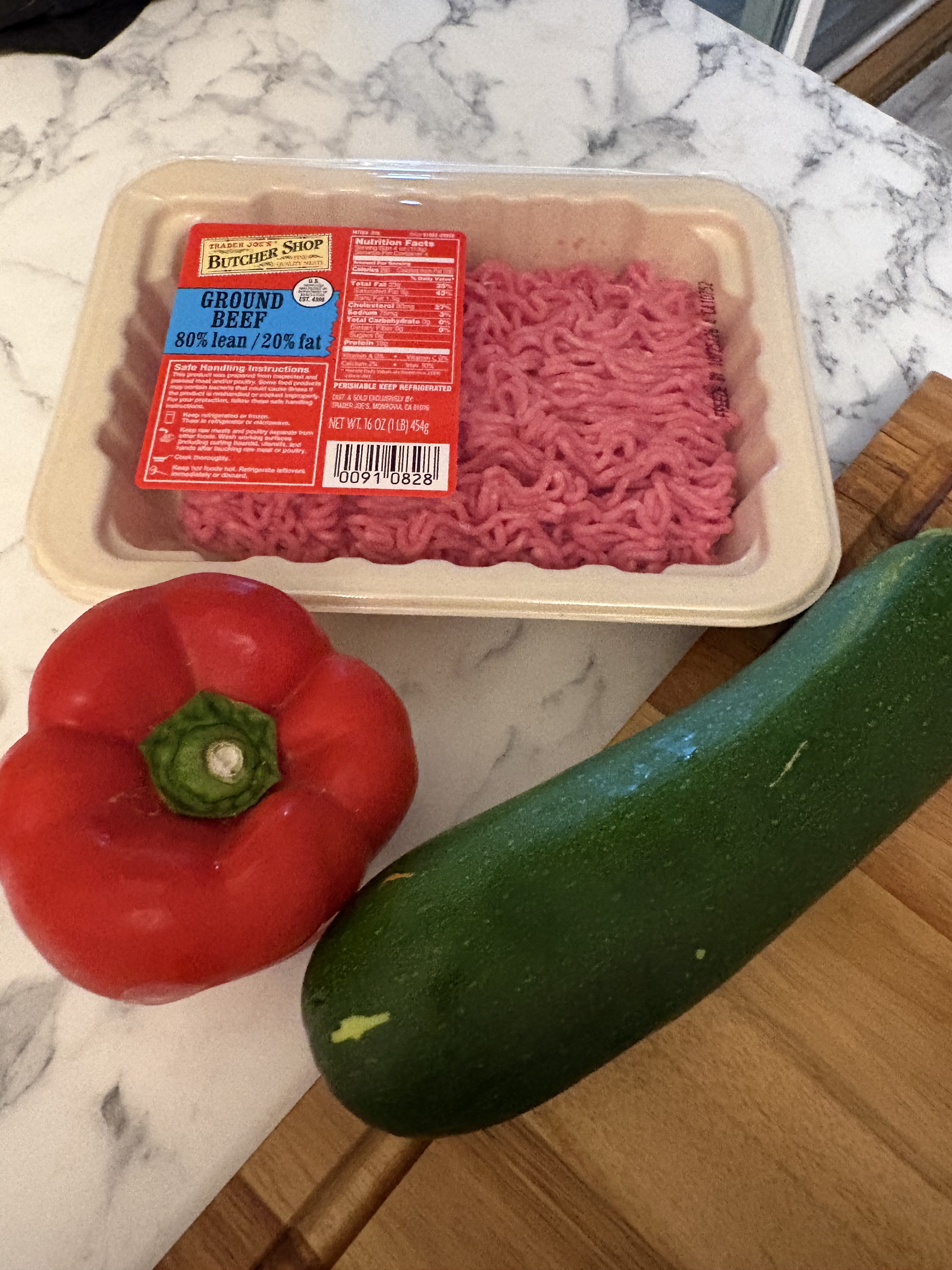 A package labeled Trader Joe’s 80 percent lean ground beef sits beside a red bell pepper and zucchini on a kitchen counter.