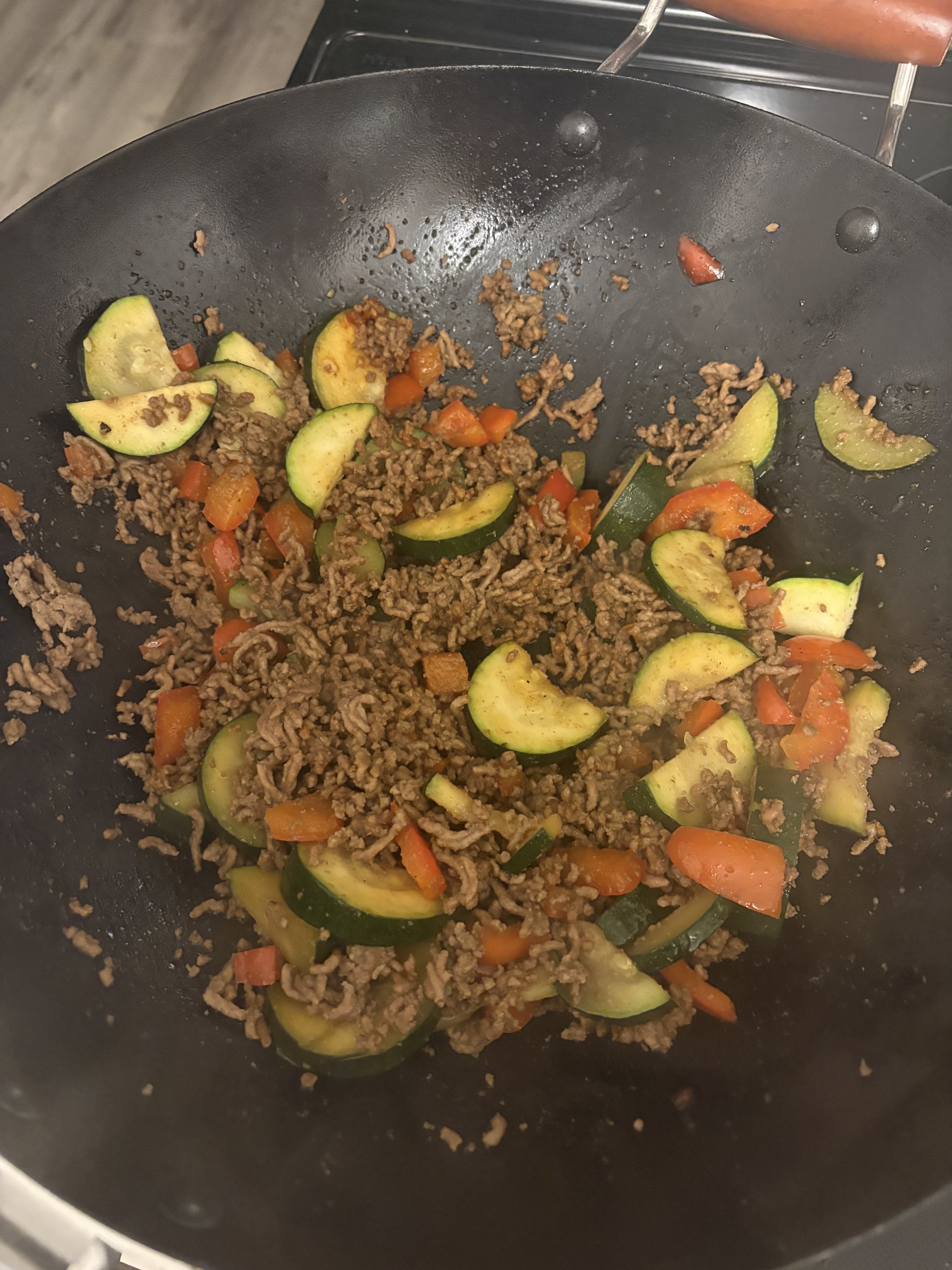Ground beef, sliced zucchini and red bell pepper cook together in a black wok.